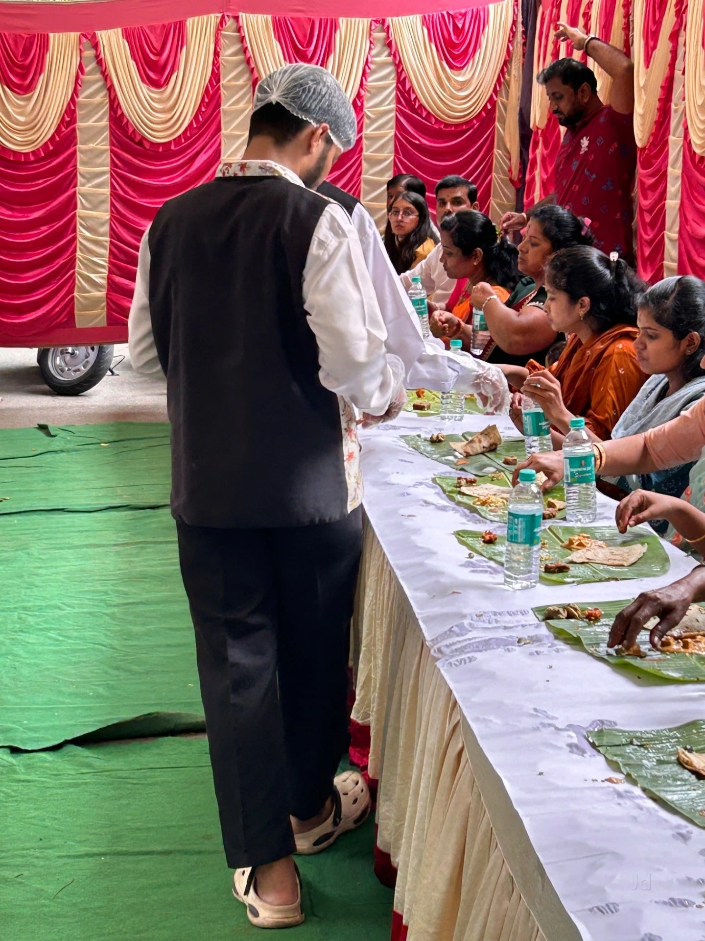 A gloved server attending to guests at a banana-leaf meal