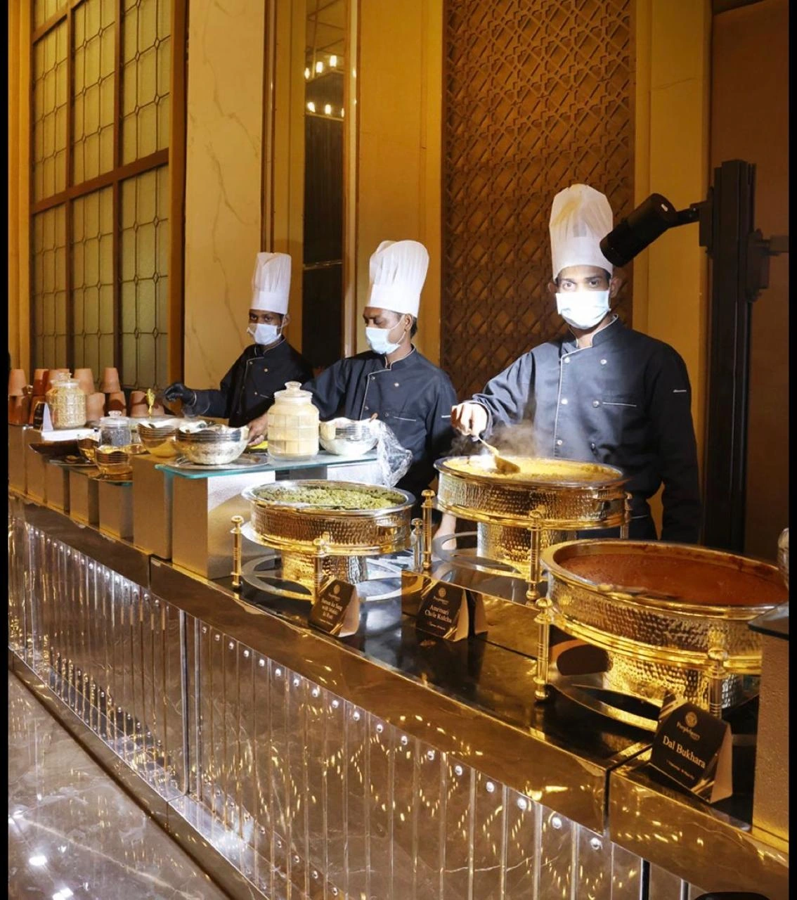 Chefs standing behind a row of polished brass buffet vessels