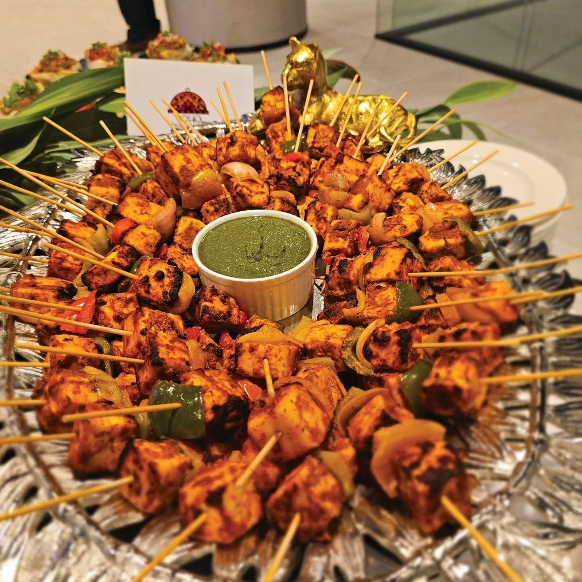Paneer skewers arranged on a silver platter around a bowl of green chutney